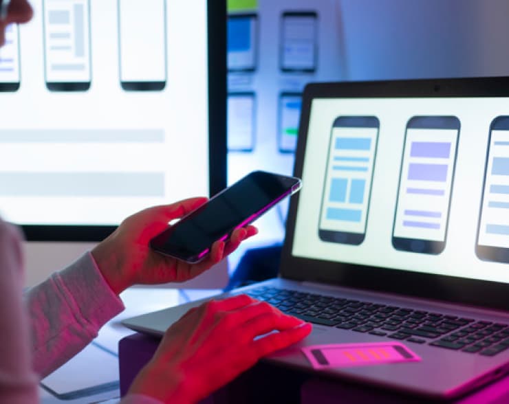 A person is looking at a smartphone in front of a laptop